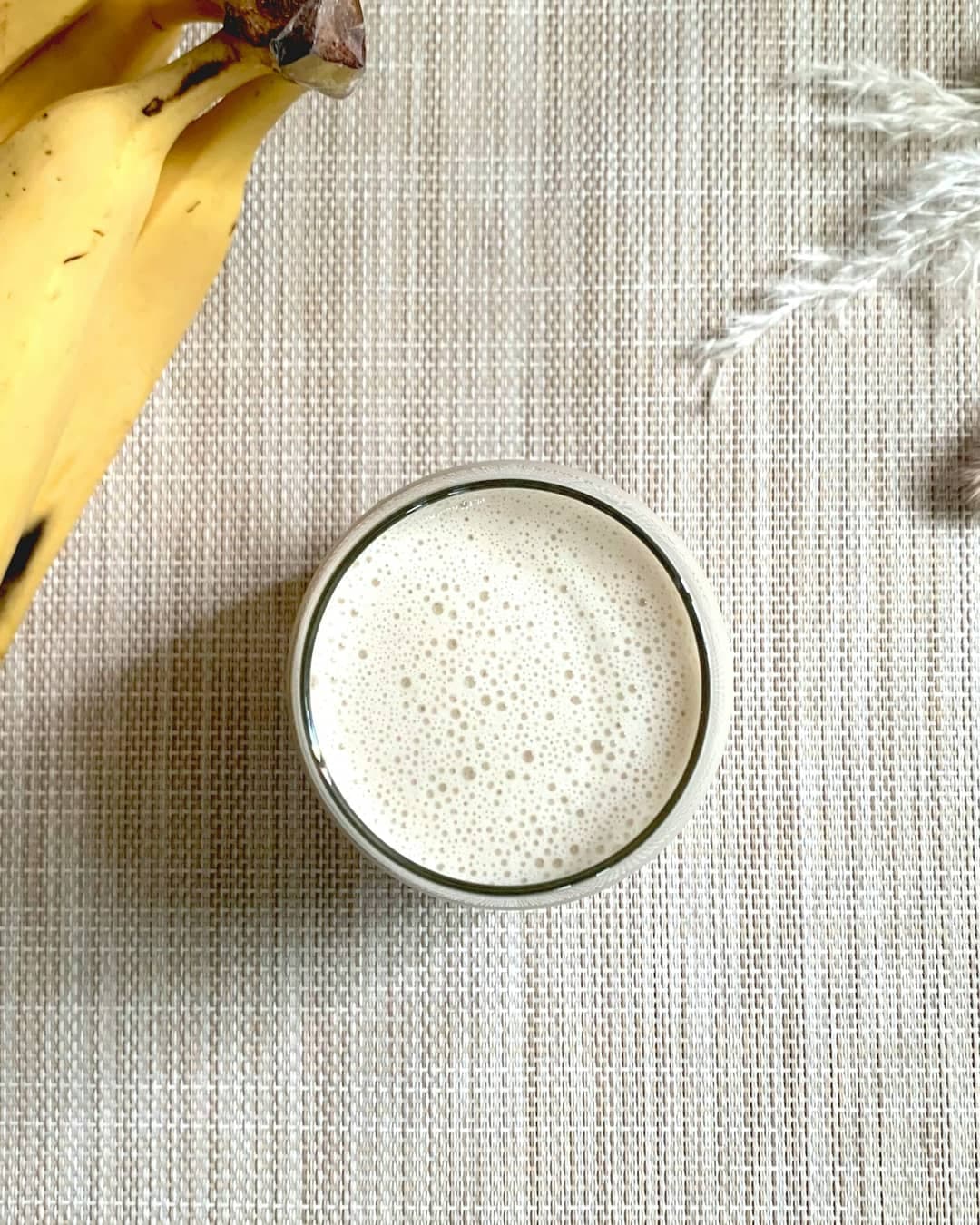 A creamy banana latte seen from above, beside fresh bananas